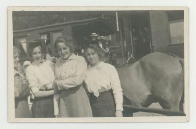 Individuals posing in front of a train with a horse drawn carriage postcard